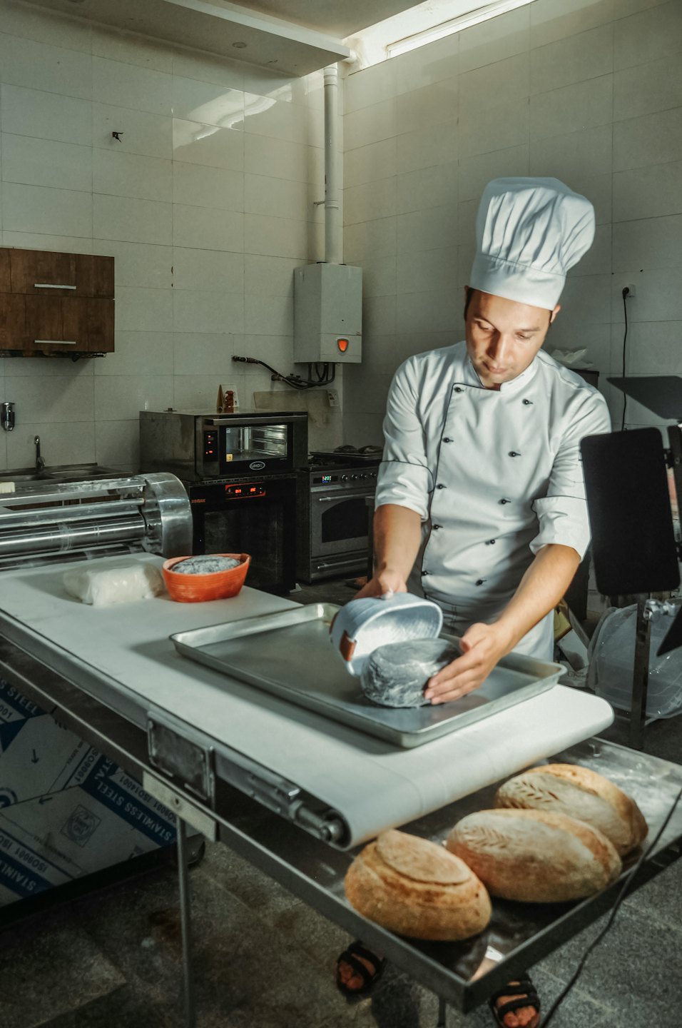 Baker places a dough ball onto a tray in a kitchen.