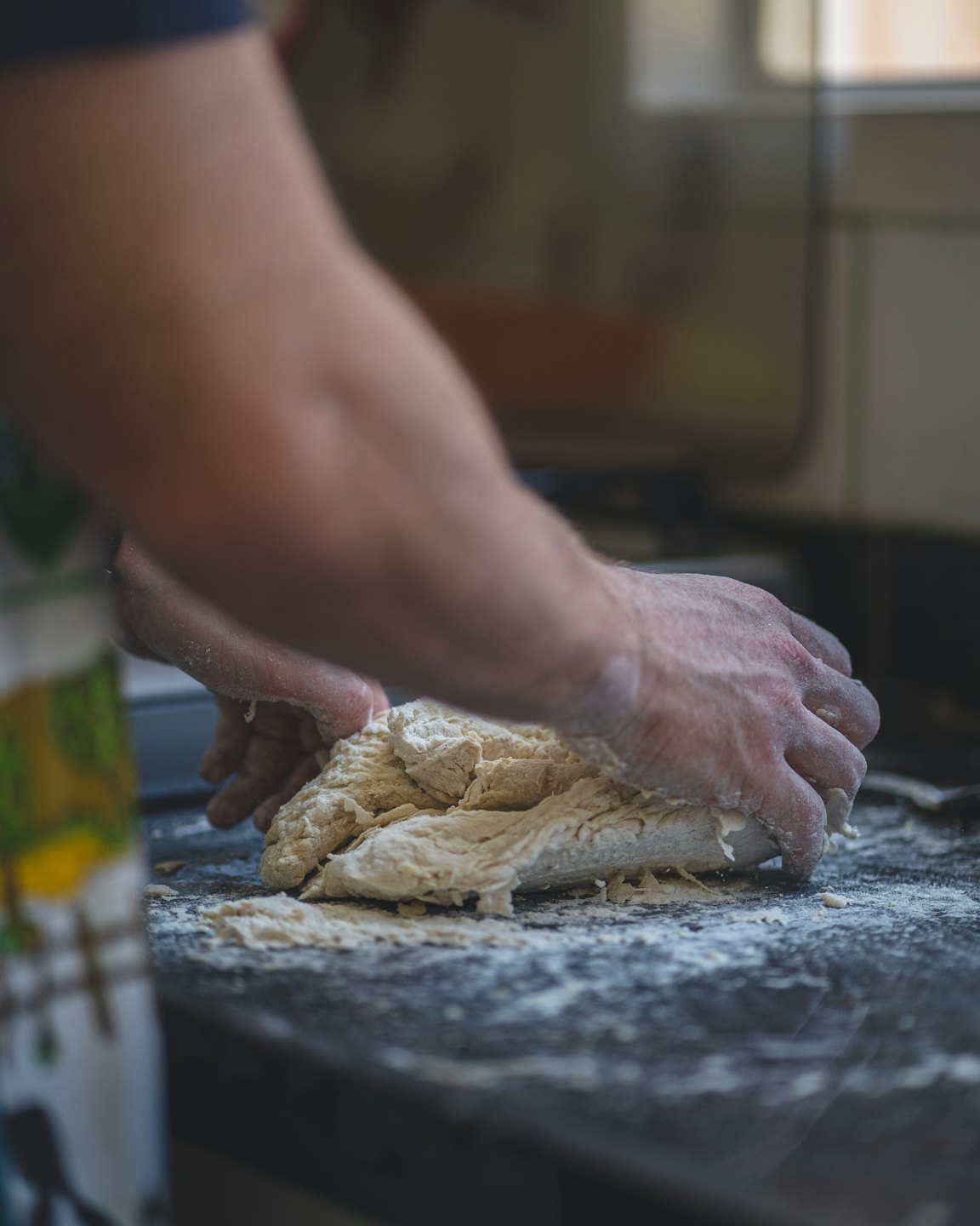 Hands kneading fresh dough on a floury kitchen counter.