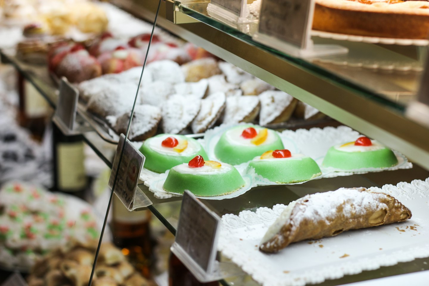 Pastries and cakes sit on doilies inside a glass display case.